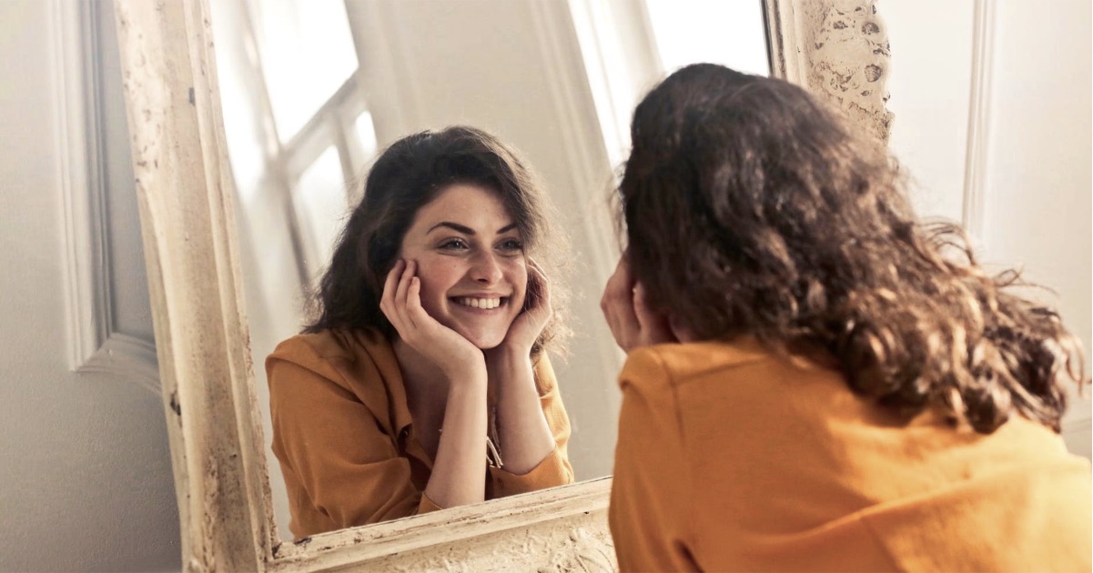 A woman smiling and admiring herself at the mirror
